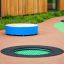 Round trampoline (100 cm) ümbritsetud pehmest pinnast laste mänguväljakul.